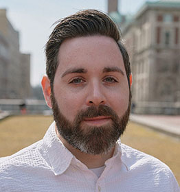Mason assistant professor Johnathan Auerbach wears a white, collared-shirt and has brown hair and a beard in his faculty profile