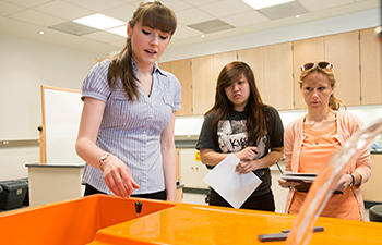 Two female engineering students observe a demonstration of fluid mechanics in the lab at the Volgenau School of Engineering at George Mason University. 
