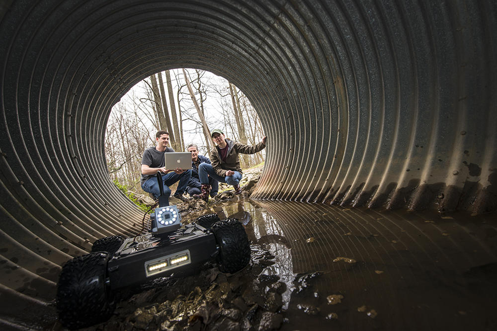 Three people at the other end of a tunnel, with a small robot moving towards the camera.