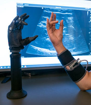 A robot arm mirroring the movements of a person's arm on the right. Both sitting on a desk. 