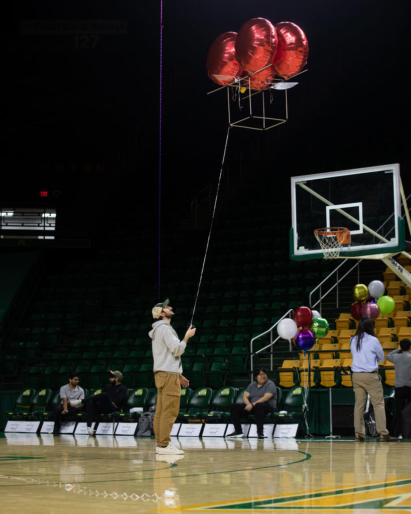A male student holds a kite-like BLIMP in the GMU basketball arena