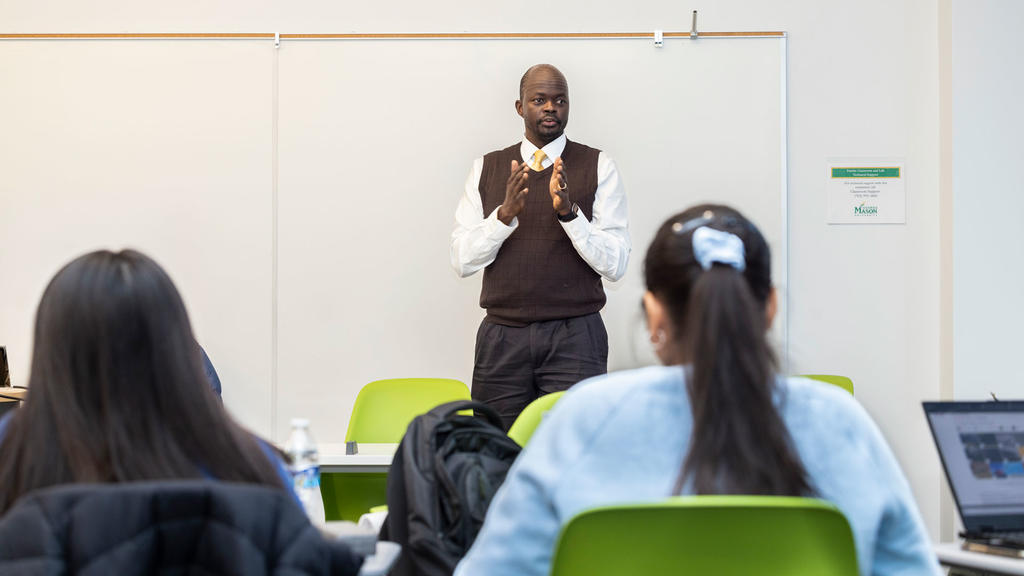 A black, male professor stands in a classroom teaching students in front of him